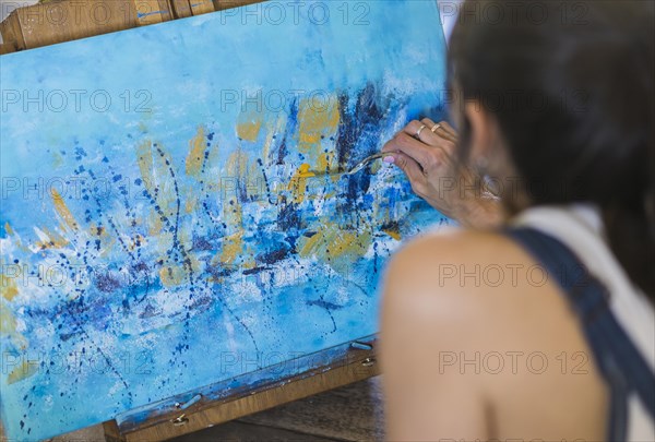 Close up of a woman painting on a canvas a blue abstract painting