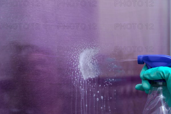 Close-up shot of a spray can of spray cleaner spraying liquid onto a glass pane