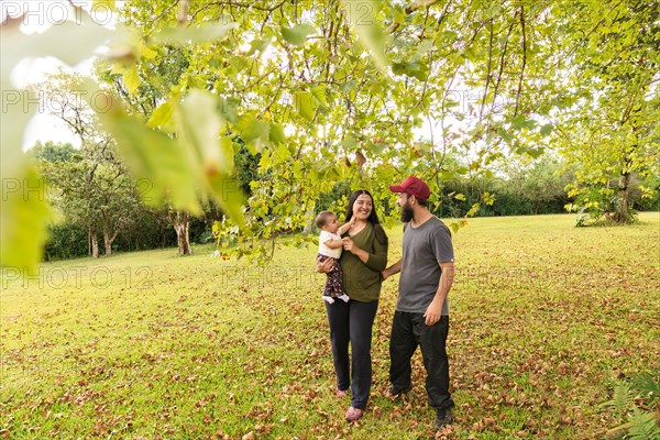 Happy Latin family. Mother and father smiling and looking at their baby girl taking a walk in the open air. The concept of a healthy lifestyle