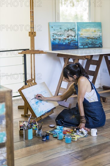 Woman artist painting on a canvas a blue abstract painting. Creative ywoman working on the floor in her art studio