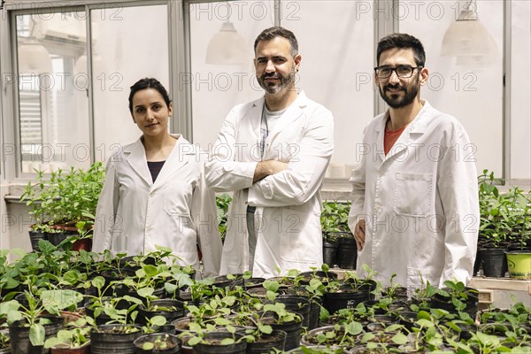 Group portrait of scientists in their lab coats looking at the camera in a greenhouse