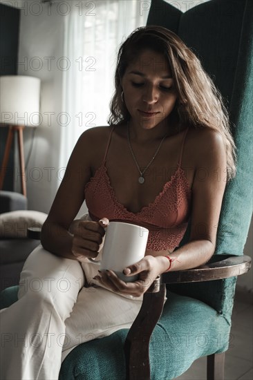 Interior shot of a beautiful Latina woman holding a cup with hot tea or coffee in the morning
