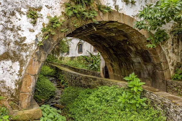 Old historical stone tunnel passing through vegetation and old colonial-style houses in the historic city of Ouro Preto in the state of Minas Gerais.