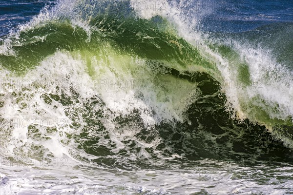 Beautiful and strong sea waves with water drops and foam splashing in the air on a sunny day