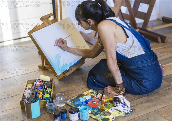 Woman artist painting on a canvas a blue abstract painting. Creative ywoman working on the floor in her art studio