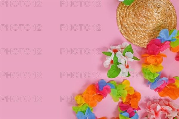 Bright flower lei necklaces and summer straw hat on side of pink background with copy space