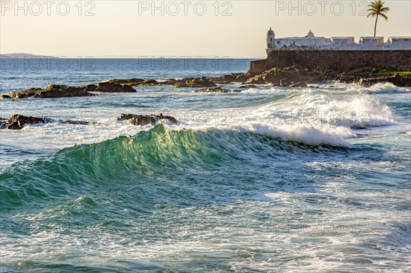 Salvador sea waves with an old colonial fortress from the empire era in the background during sunset.