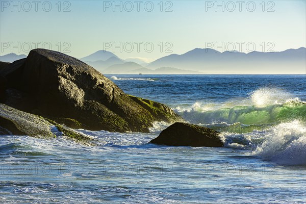 Waves crashing against the rocks at summer dawn on Devil beach in Ipanema Rio de Janeiro with mountains at background