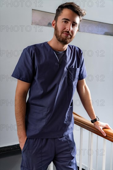 Young smiling young male doctor dentist in dark blue uniform standing in hallway