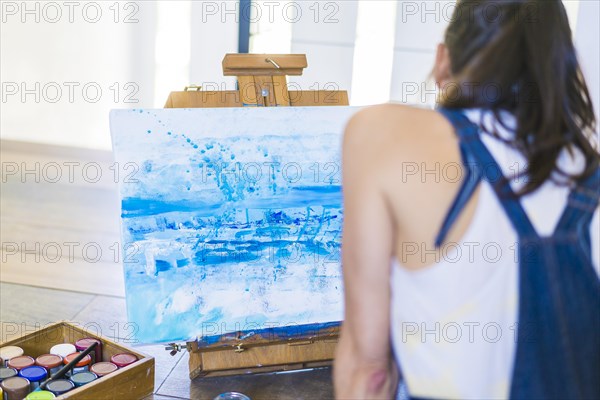 Woman artist painting on a canvas a blue abstract painting. Creative ywoman working on the floor in her art studio