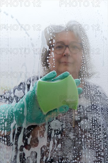 A woman cleans the glass with a green sponge and gloves