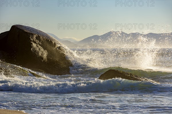 Waves crashing against the rocks at summer dawn on Devil beach in Ipanema Rio de Janeiro with mountains at background