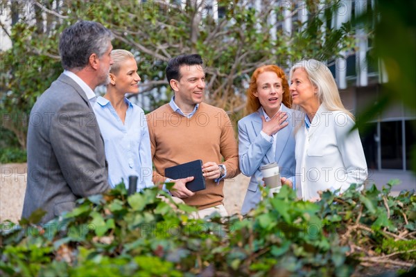 Talking next to a green area of the business area. Group executives or businessmen and businesswoman in a business area