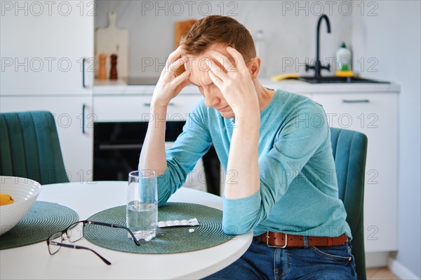 Sick middle aged man in the kitchen massaging head