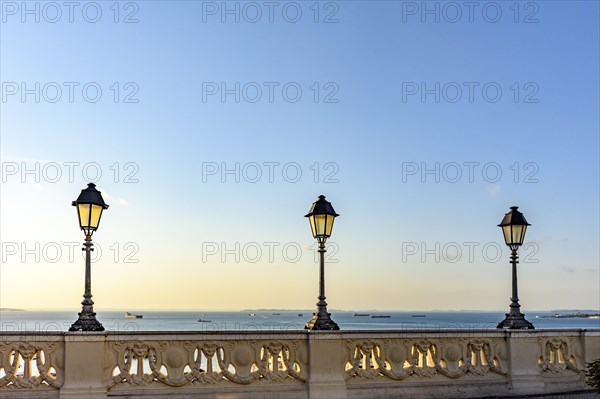 Old colonial style lanterns lighting on walls in the streets of Salvador with the All Saints bay in the background with their boats during the sunset