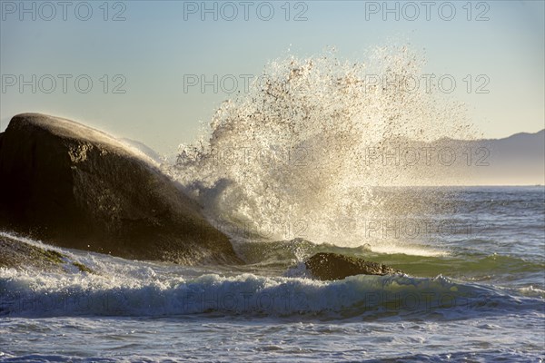 Waves crashing against the rocks at summer dawn on Devil beach in Ipanema Rio de Janeiro with mountains at background