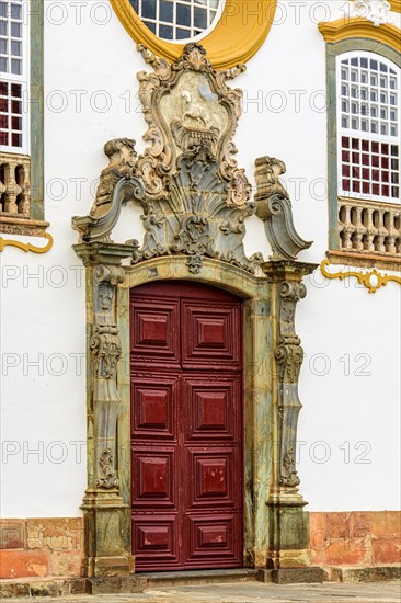 Door of an old church in baroque style with carved stone frame and decorated with images and symbols in the historic city of Tiradentes in Minas Gerais