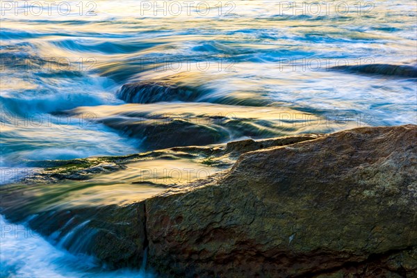 Sea water blurred by the movement and dripping between the stones with the colors and brightness of the sunset on Ipanema beach in Rio de Janeiro
