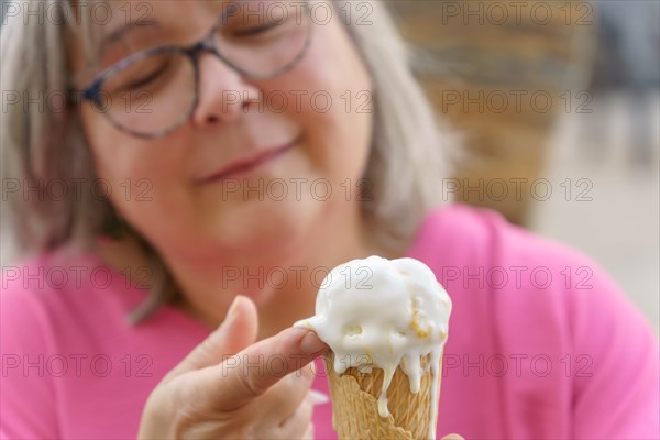 Close-up of a white-haired woman with glasses eating an ice cream with her fingers