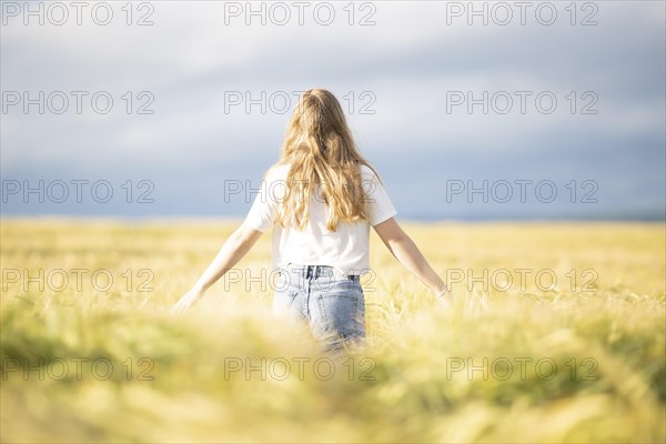 A young girl walks through a cornfield on a sunny warm day and spreads out her arms