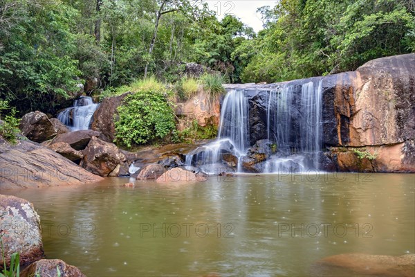 Waterfall and lake in rain forest of Moeda in Minas Gerais state on cloudy day among rocks and vegetation