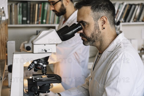 Scientist viewing sample through microscope during experiment in laboratory