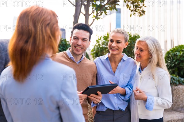 Cheerful group of coworkers laughing and looking at a tablet outdoors in a corporate office area