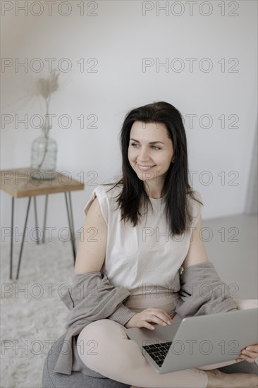 Young woman sitting comfortably with laptop on a stool in the living room