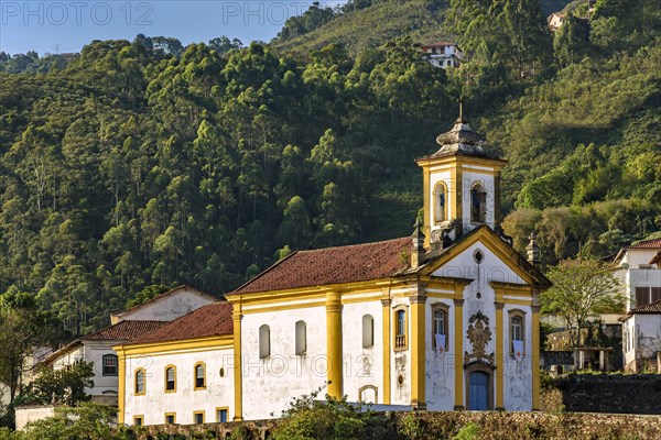 Facade of a historic baroque-style church in the city of Ouro Preto in Minas Gerais illuminated during the late afternoon with the hills and local vegetation