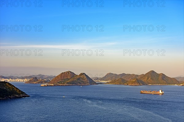 Cargo ship arriving at the entrance of the Guanabara Bay in Rio de Janeiro with Niteroi city in background at afternoon