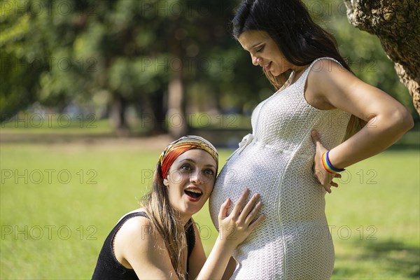 Young woman listening to his beautiful pregnant girlfriend's tummy and smiling