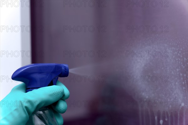 Close-up shot of a spray can of spray cleaner spraying liquid onto a glass pane