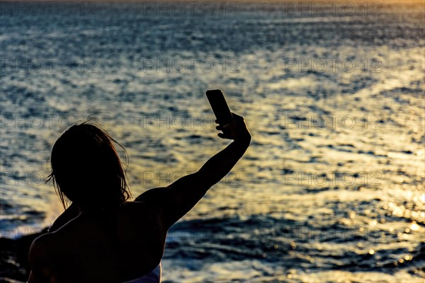 Silhouette of girl with smartphone taking selfie in the summer during the sunset in Salvador city