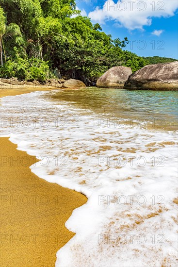 Sea foam advancing over the sand on the beach surrounded by rainforest in Ilha Grande