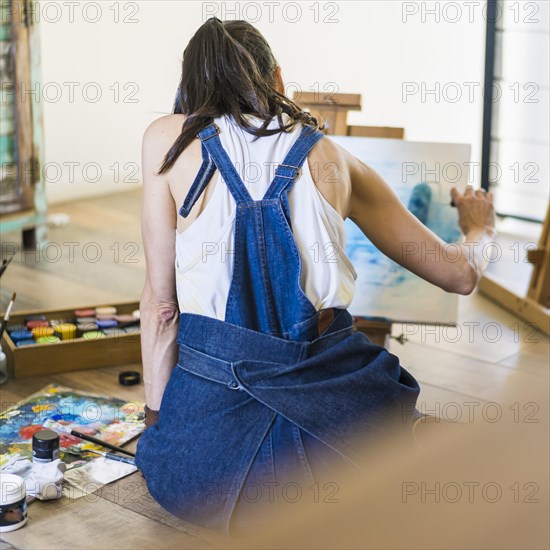 Woman artist painting on a canvas a blue abstract painting. Creative ywoman working on the floor in her art studio