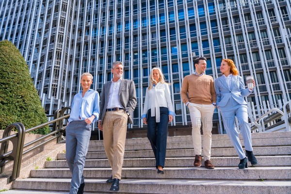 Cheerful group of coworkers outdoors in a corporate office area walking down some stairs going to work