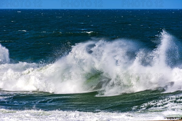 Beautiful and strong atlantic sea waves with water drops and foam splashing in the air on a blue sunny day