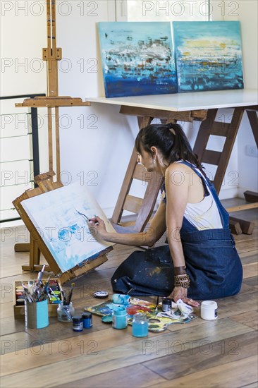 Woman artist painting on a canvas a blue abstract painting. Creative ywoman working on the floor in her art studio