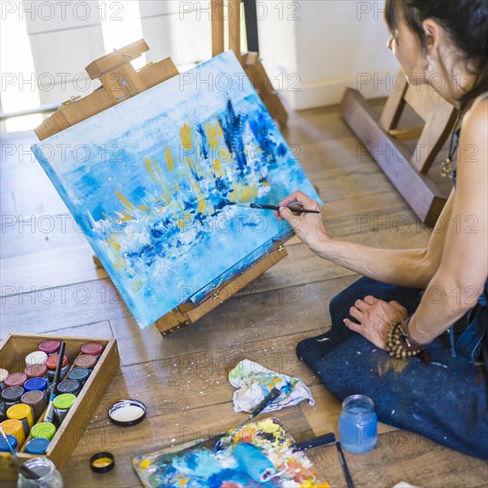 Woman artist painting on a canvas a blue abstract painting. Creative ywoman working on the floor in her art studio