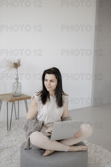 Young woman sitting comfortably with laptop on a stool in the living room