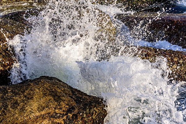 Water and sea foam splashing in the air with waves crashing against rocks