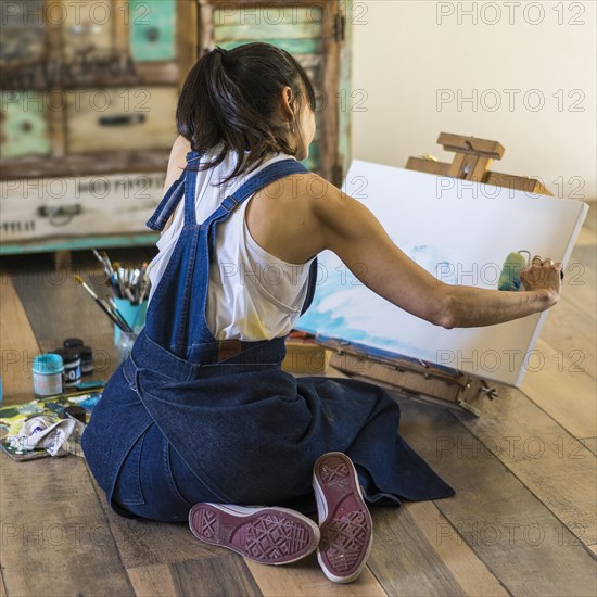 Woman artist painting on a canvas a blue abstract painting. Creative ywoman working on the floor in her art studio