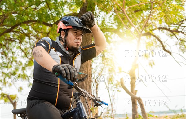 Tired cyclist while riding the bike on a road. Exhausted chubby cyclist on his bike looking into the distance