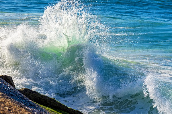 Wave breaking against beach rocks in the summer morning sun