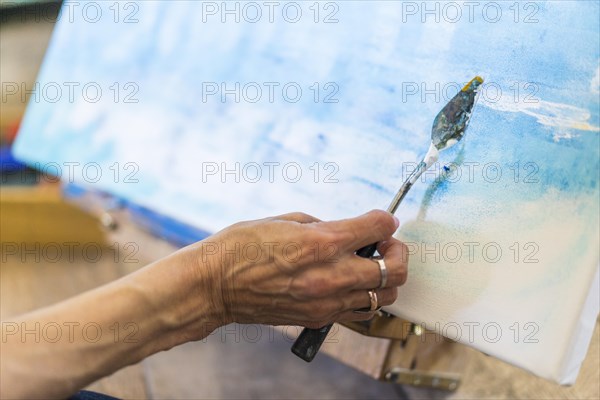 Close up of a woman's hand painting on a canvas a blue abstract painting