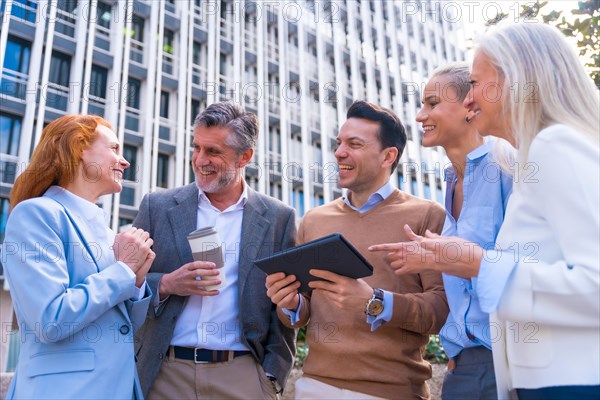 Cheerful group of coworkers laughing and looking at a tablet outdoors in a corporate office area