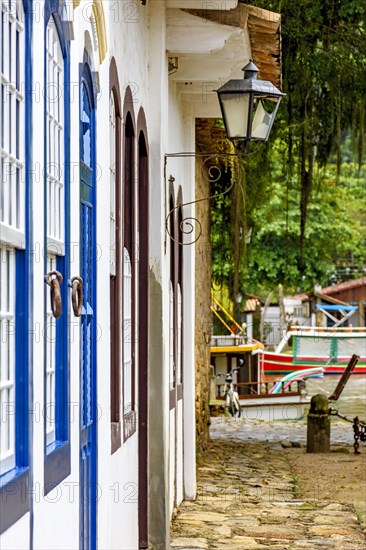 Colonial style house facades with old metal lantern and boats in the background in the historic town of Paraty