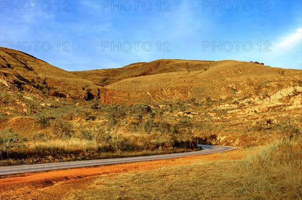 Empty road between the hills with stones and vegetation during sunset