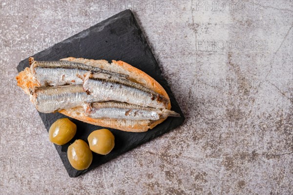 Tapa of sardines on a slice of bread with tomato and olives on black slate typical Spanish
