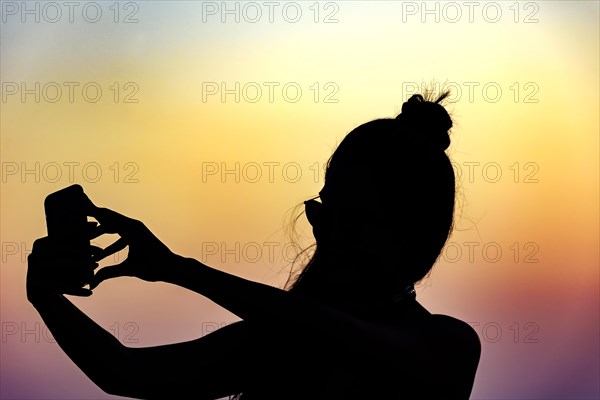 Silhouette of girl with smartphone taking selfie in the summer during the sunset